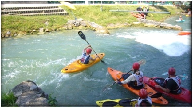 Training am Kanal in Hüningen: Ein Jugendlicher mit gelbem Boot fährt in eine Schwelle, drei andere Paddler*innen stehen im Kehrwasser daneben und schauen, wie er durchfährt